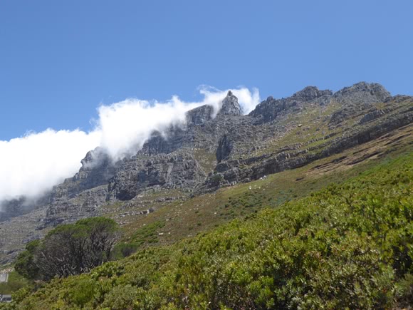 View up a mountain side with clouds coming over the mountain ridge
