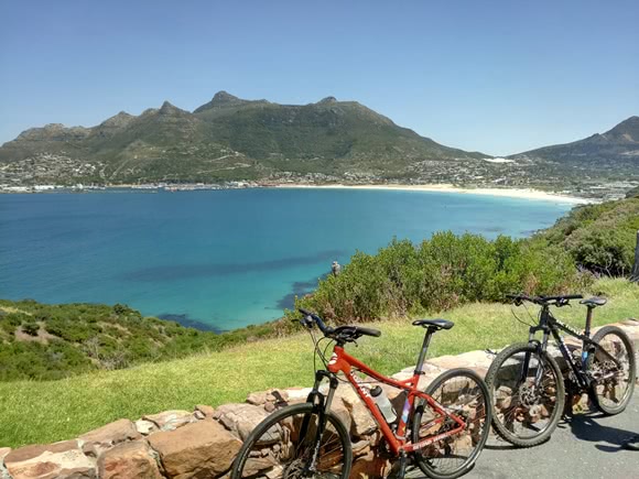 Two bikes resting on a brick wall with the sea and mountains in the background